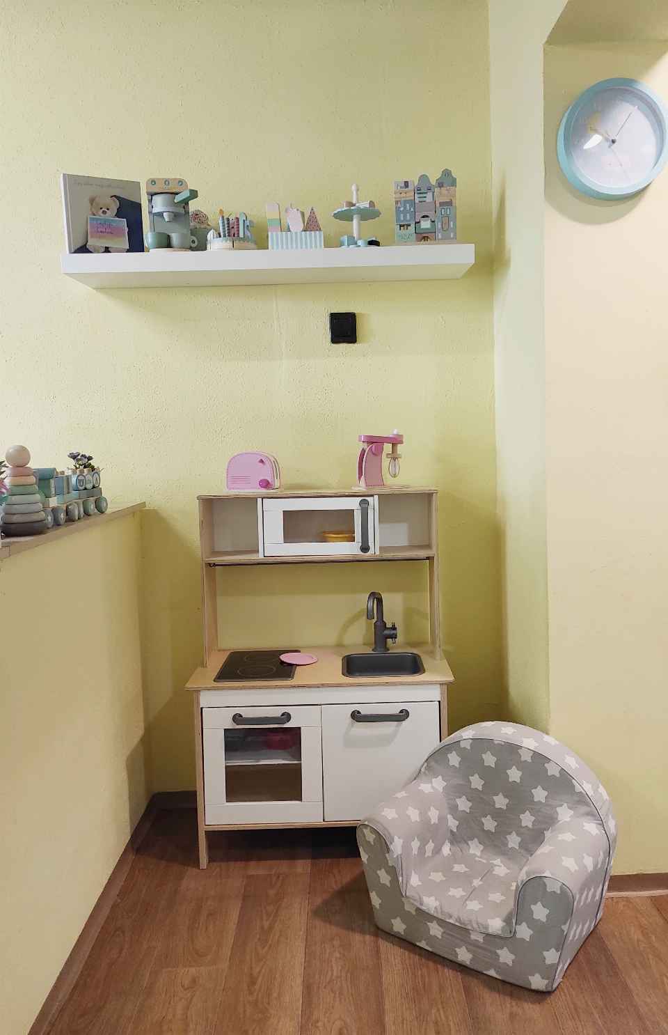 Játékkonyha és gyerekfotel egy sárga falú játszósarokban